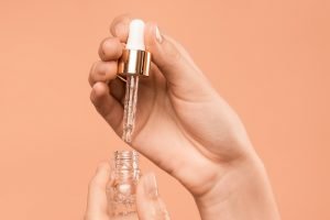 hands holding small serum bottle with peach backdrop